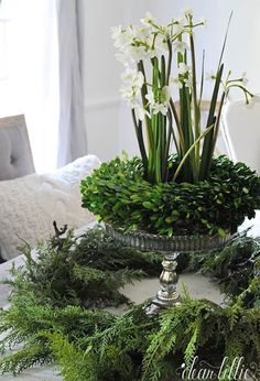 a glass bowl filled with white flowers and greenery on top of a dining room table