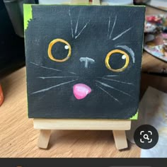 a black cat painted on an easel with yellow eyes and pink tongue is shown