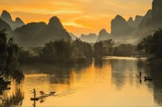 a person in a small boat on a river at sunset with mountains in the background