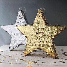 two gold and silver stars are sitting next to each other on a table with confetti