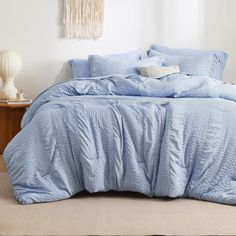 a bed with blue comforter and pillows in a white room next to a table