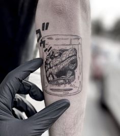 a man with a tattoo on his arm holding up a jar filled with something in it