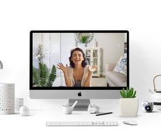 a desktop computer with a woman on the screen and various office supplies around it, including a potted plant