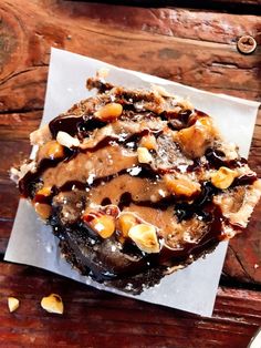 a chocolate dessert with nuts on top of it sitting on a piece of parchment paper