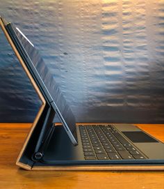 an open laptop computer sitting on top of a wooden table next to a blue wall