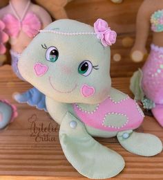 a stuffed animal that is sitting next to other stuffed animals on a wooden surface with pink and green colors