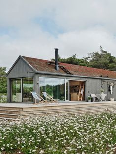 a house with an outdoor deck in the middle of some grass and flowers around it