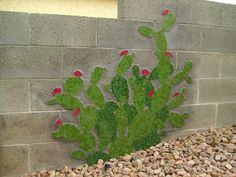 a green cactus painted on the side of a brick wall next to gravel and rocks