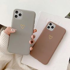 two phone cases with heart stickers on them, one is gray and the other is brown