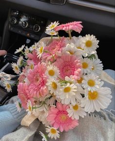 a bouquet of pink and white daisies in someone's lap with the steering wheel behind them