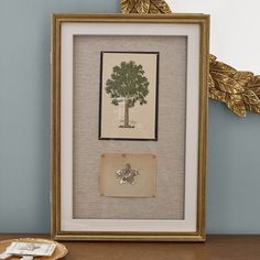 a framed picture with a tree on it next to a plate and gold leaf decoration