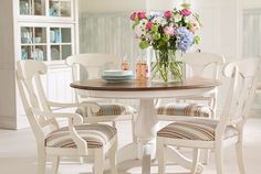 a dining room table and chairs with flowers in vase