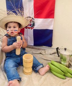 a small child wearing a straw hat and holding a wooden toy in front of a flag