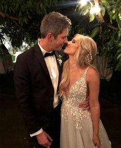 a man in a tuxedo kissing a woman in a gown under a tree