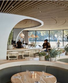 people sitting at tables in a restaurant with lots of windows and plants on the counter