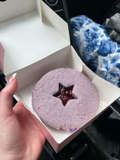 a person holding up a purple cake in a box