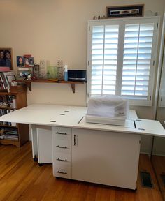 a white desk with drawers and a laptop computer on it in front of a window