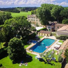 an aerial view of a pool surrounded by lush green trees and lawns in front of a large mansion