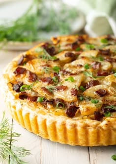 a quiche with bacon, cheese and green onions on a white wooden table next to fresh herbs