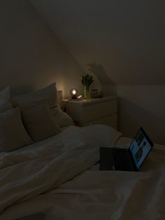 a laptop computer sitting on top of a bed in a room with white sheets and pillows