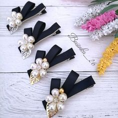 four hair clips with flowers and pearls on them sitting on a white wooden surface,