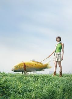 a woman is pulling a fish on a leash through the grass with her hand and head