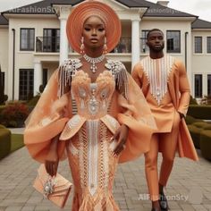 two people standing in front of a large house wearing orange dresses and headpieces