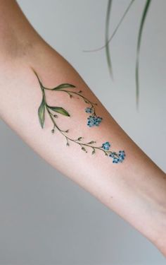 a woman's arm with blue flowers and green leaves on the left side of her arm