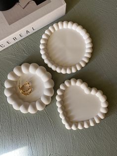 three small white plates sitting on top of a table next to a box with a ring in it