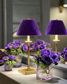 two purple lamps are sitting on a table with flowers in vases next to them