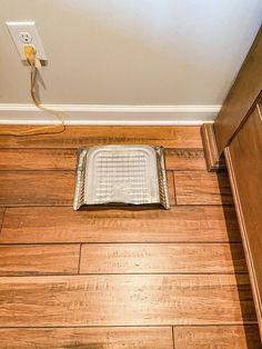 a wooden floor with a grate on the ground in front of an electrical outlet