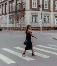 a woman crossing the street in front of an old building and holding a handbag