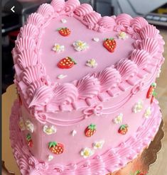 a pink heart shaped cake with strawberries on it sitting on top of a wooden table