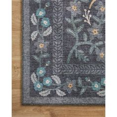 an area rug with blue flowers and leaves on the side, in front of a wooden floor