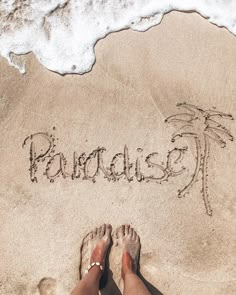 someone is writing paradise in the sand at the beach with their feet on the shore