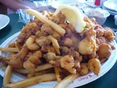 fried food on a plate with french fries and lemon wedges