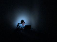 a person in the dark with a laptop computer on their lap and head turned to the side