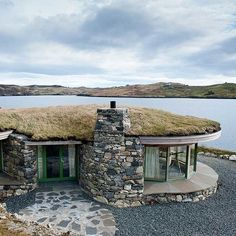 a house made out of rocks with grass on the roof and windows that look like they are floating in water