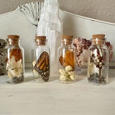 four glass bottles filled with different types of flowers and butterflies on top of a table