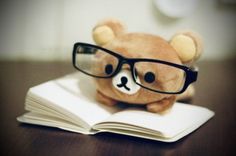 a teddy bear wearing glasses sitting on top of an open book