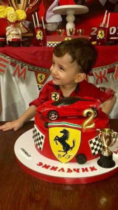 a young boy sitting in front of a red and white cake with ferrari on it