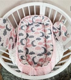 a baby crib with pink and gray clouds on it's back, next to a teddy bear pillow