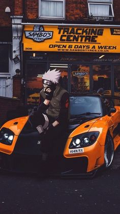 a man sitting on top of an orange sports car in front of a racing centre