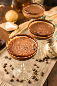 two glasses filled with chocolate drink sitting on top of a table next to coffee beans