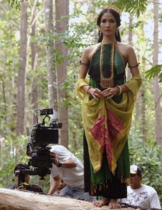 a woman standing on top of a wooden log in the woods next to a camera