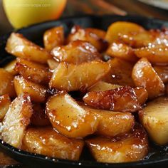 some fried food in a black bowl on a table next to an orange and apple