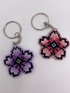 two cross stitch keychains with flower designs on them, one is purple and the other is pink