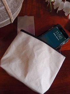 a cell phone sitting inside of a white pouch on top of a wooden table next to flowers