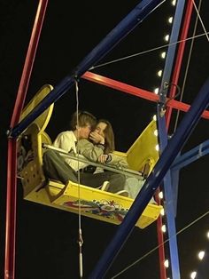 a man and woman sitting on a swing ride at an amusement park during the night