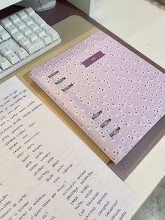 a pink binder sitting on top of a desk next to a keyboard